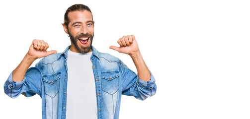 Attractive man with long hair and beard wearing casual denim jacket looking confident with smile on...