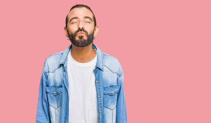 Attractive man with long hair and beard wearing casual denim jacket looking at the camera blowing a kiss on air being lovely and sexy. love expression.