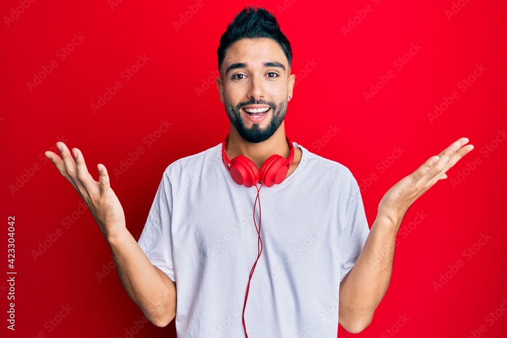 Wall mural young man with beard listening to music using headphones celebrating crazy and amazed for success wi