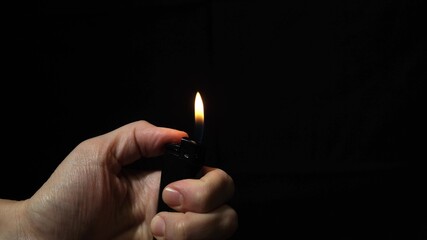 Hand burning flame with a lighter in the dark, black night background, portable device used to create a flame