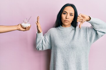 Young hispanic girl rejecting bowl with sugar with angry face, negative sign showing dislike with...