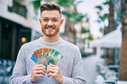 Young caucasian man smiling happy holding australian dollars at the city.