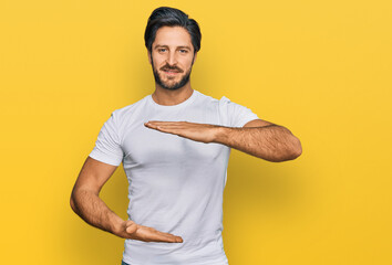 Young hispanic man wearing casual white t shirt gesturing with hands showing big and large size sign, measure symbol. smiling looking at the camera. measuring concept.