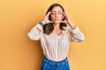 Young brunette woman wearing casual clothes over yellow background with hand on head, headache because stress. suffering migraine.