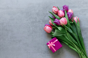 Pink gift box and tulips on a gray concrete background. Copyspace. Postcard. Gift