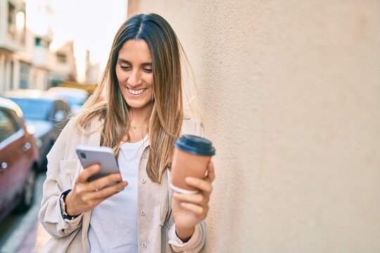 Young caucasian woman smiling happy using smartphone and drinking take away coffee at the city.