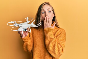Young blonde woman holding drone covering mouth with hand, shocked and afraid for mistake....