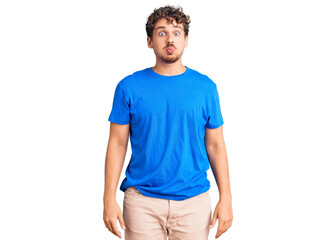 Young handsome man with curly hair wearing casual clothes puffing cheeks with funny face. mouth...