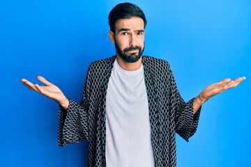 Young hispanic man wearing casual clothes clueless and confused with open arms, no idea and...