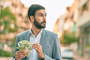 Young hispanic businessman with serious expression counting hong kong dollars banknotes at the city.