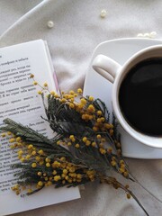 Obraz na płótnie Canvas a cup of coffee, an open book and a branch of mimosa
