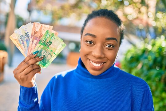 Young african american woman smiling happy holding south african rands banknotes at the park.