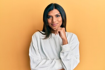 Young latin transsexual transgender woman wearing casual clothes smiling looking confident at the camera with crossed arms and hand on chin. thinking positive. - obrazy, fototapety, plakaty