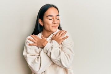 Young asian woman wearing casual sweatshirt hugging oneself happy and positive, smiling confident. self love and self care
