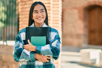 Young latin student girl smiling happy holding folder at the city.