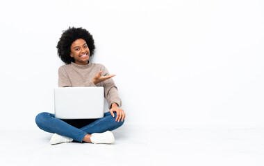 Young African American woman with a laptop sitting on the floor presenting an idea while looking...