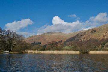 Sunny spring / winter day on a reed fringed lake; brown and red bracken coated mountains beneath...