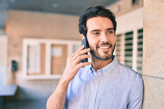 Young hispanic man smiling happy talking on the smartphone leaning on the wall