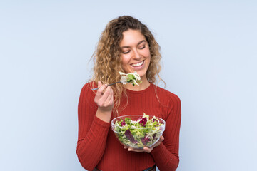 Young blonde woman with curly hair holding a salad over isolated wall