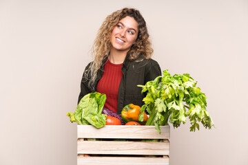 Farmer with freshly picked vegetables in a box isolated on beige background laughing and looking up