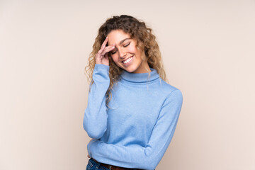 Young blonde woman with curly hair wearing a turtleneck sweater isolated on beige background laughing