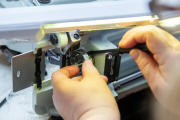 Female hands with a screwdriver repair the shuttle of the sewing machine.
