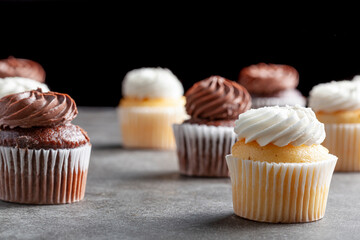 Side view image of vanilla and chocoloate cupcakes on dark stone countertop against black background. Concept for parties, celebration and late night snack