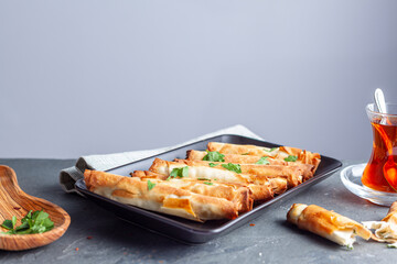 Traditional Turkish sigara boregi, a phyllo dough roll with cheese or ground meat stuffing. Deep fried rolls are served on a tray with parsley leaves as topping and Turkish tea on the side.