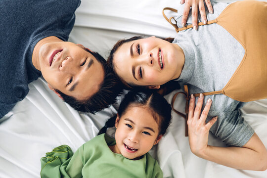 Top view of portrait enjoy happy smiling love asian family father and mother with young parents little asian daughter girl looking at camera in moments good time lying on the floor at home