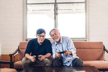 Portrait of happy love asian family senior mature father and young man adult son having fun enjoy holding gamepad controller play console video game together at home
