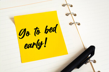 Closeup Yellow Sticky Note paste it in a notebook setting an appointment. The words Go to bed early written on a white notebook to remind you an important appointment.