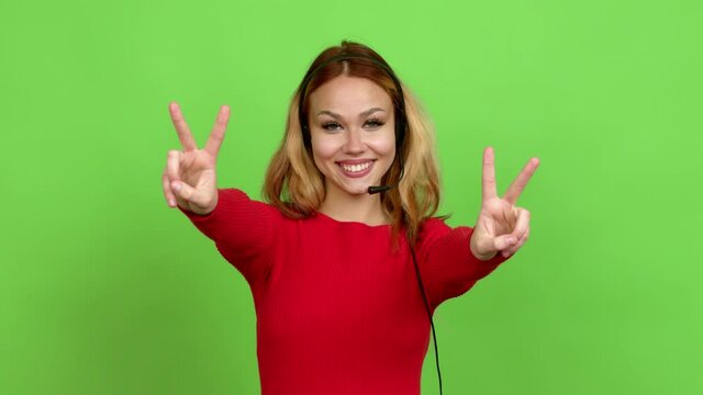 Young blonde teenager girl telemarketer smiling and showing victory sign with a cheerful face over isolated background. Green screen chroma key