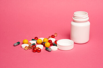 White jar with multi-colored pills on a pink background close-up