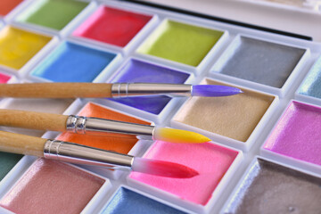 A close up image of brightly colored water paints and paint brushes.  
