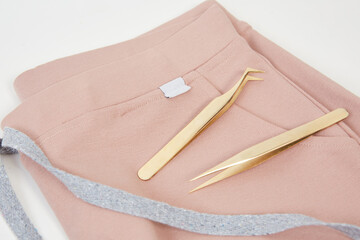 closeup set of tweezers for depilation on a pink surgical uniform on a white background