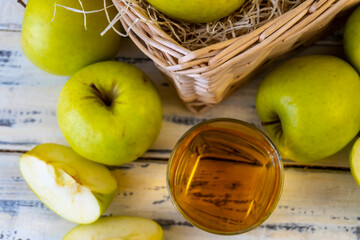 Green apples, glass with apple juice and basket with apples on wooden background