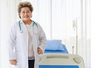 Portrait beautiful asian senior doctor elderly woman wearing uniform and carrying stethoscope on neck smiling look happy, comfortable and healthy standing near bed and look at camera at hospital