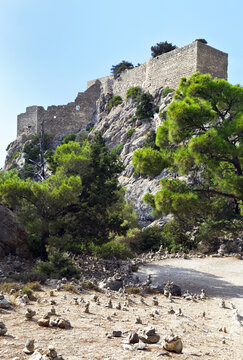 Greece. Rhodes Island. The stone walls of a medieval knight's fortified castle Monolithos (1476) and the tourist stone pyramids on the uphill path. Famous tourist attraction of the island