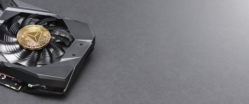 Golden TRON (TRX) coin cryptocurrency on a Black video Card on a gray background, copy space. Bitcoin mining concept. Banner