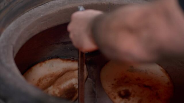 There is preparing process of pitta bread in tandoori. Traditional oriental flat bread. Baker is removing the pitta bread from tandoori wall, close-up 