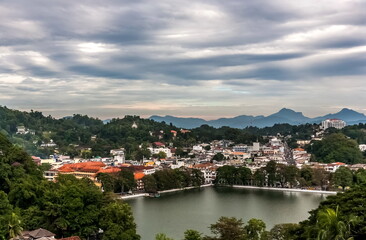 Fototapeta na wymiar Mountain view of the city pond and buildings of Kandy city against the overcast sky in Sri Lanka