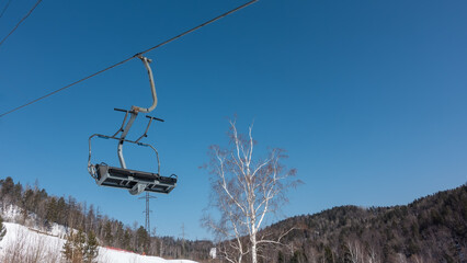 An empty cabin of a chairlift on a cable, against a background of blue sky. Close-up. Around - a...