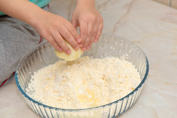 Hands of a child squeezing a lemon on the ingredients of a cake