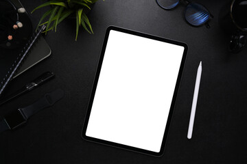 Mock up image of digital tablet with blank screen, stylus pen, smart watch, glasses and notebook on modern dark workplace.