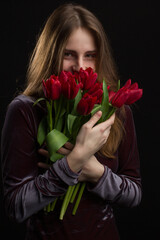 Studio portrait of a young woman on black background with a bouquet of red tulips in her hands