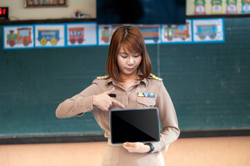 Thai teacher standing in the classroom pointing at tablet