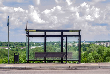 Empty public transport stop in summer. Self-isolation. Bus and minibus stops. Glass stop with a bench and a trash can. Stop without people, without passengers. bus stop sign