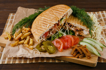 Fresh hot fragrant shawarma cut lies on a wooden board with vegetables, green leaves and fries