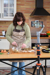 Young woman cooking stuffed aubergines and recording a video with her smartphone for her cooking channel. Content creator and influencer.