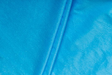 Colored blue textile satin fabric folded in folds and waves with highlights and texture